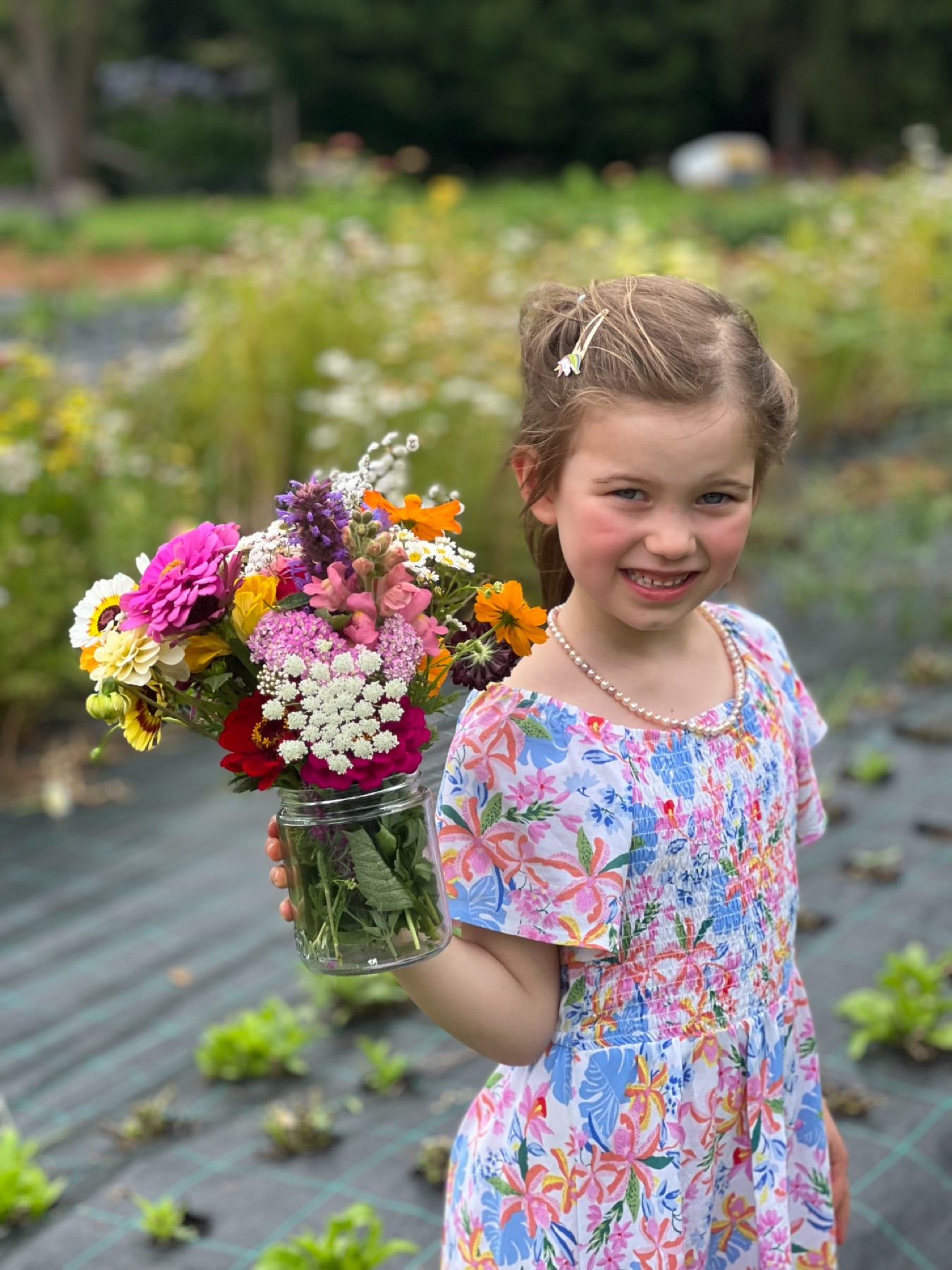 A child in the field holding a jar of picked flowers