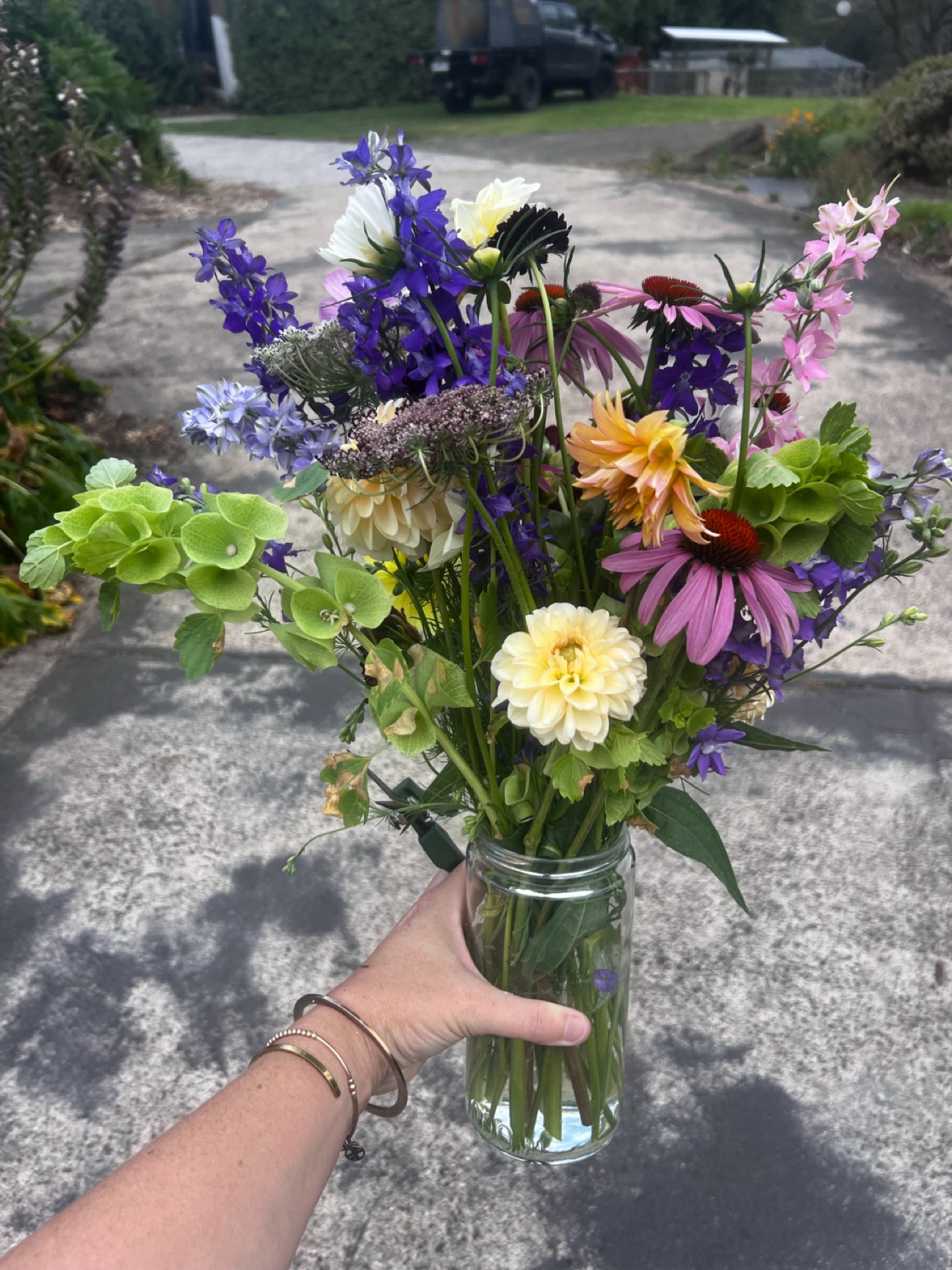 A picked jar of summer flowers held up on the driveway