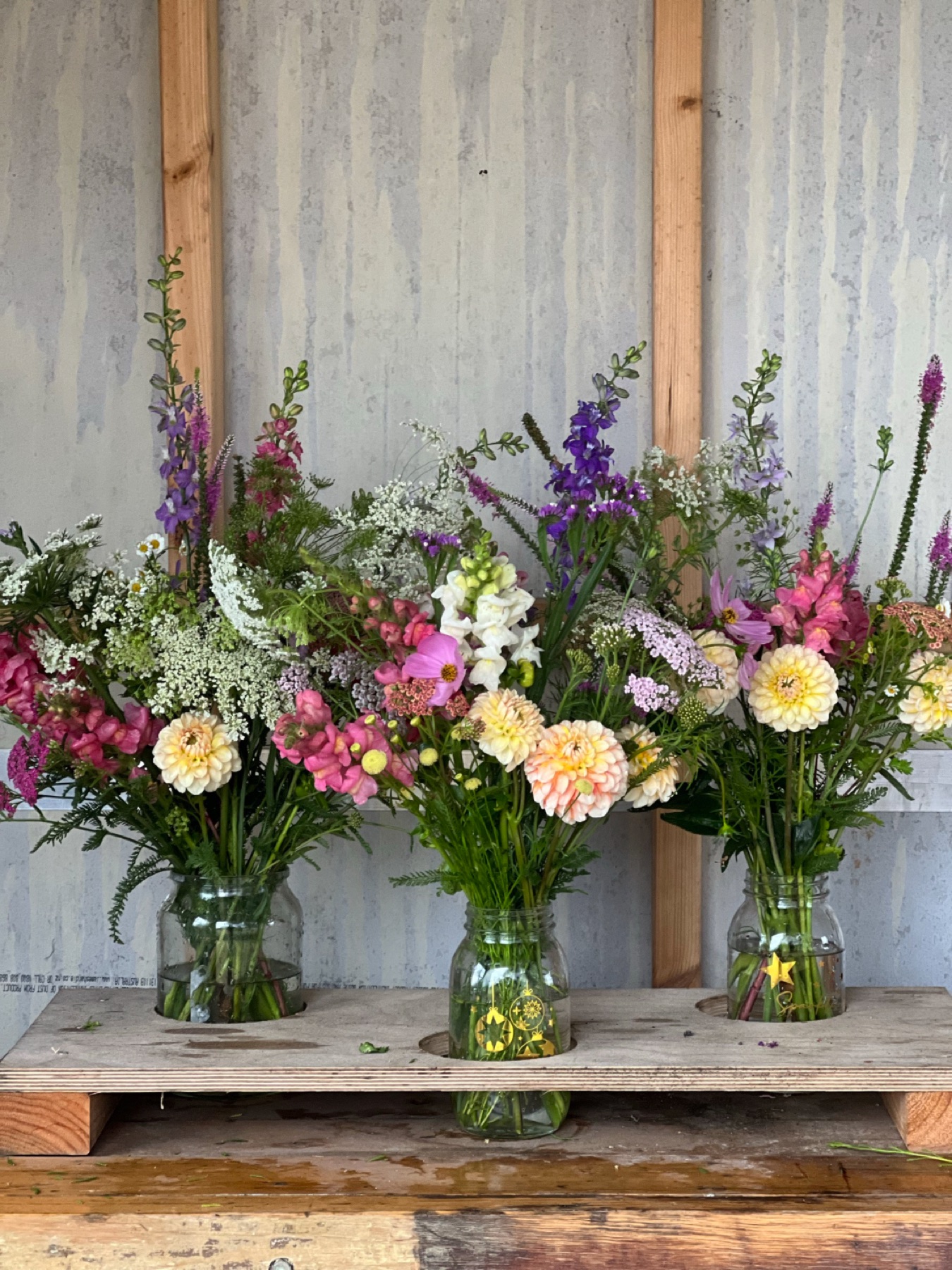 Three jars of mixed flowers on the shed bench